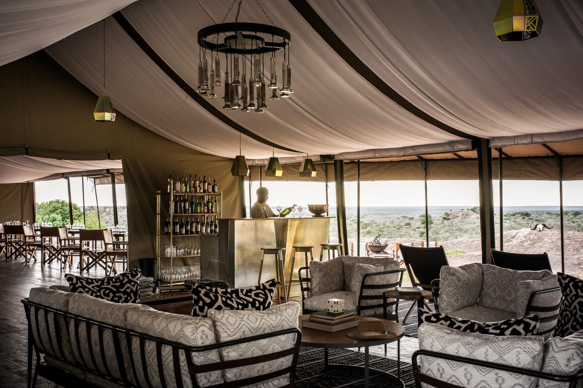 A luxe interior of a tented camp in the Serengeti complete with draping material from the roof, a bar, chandelier, and views across the surrounding bush | Go2Africa