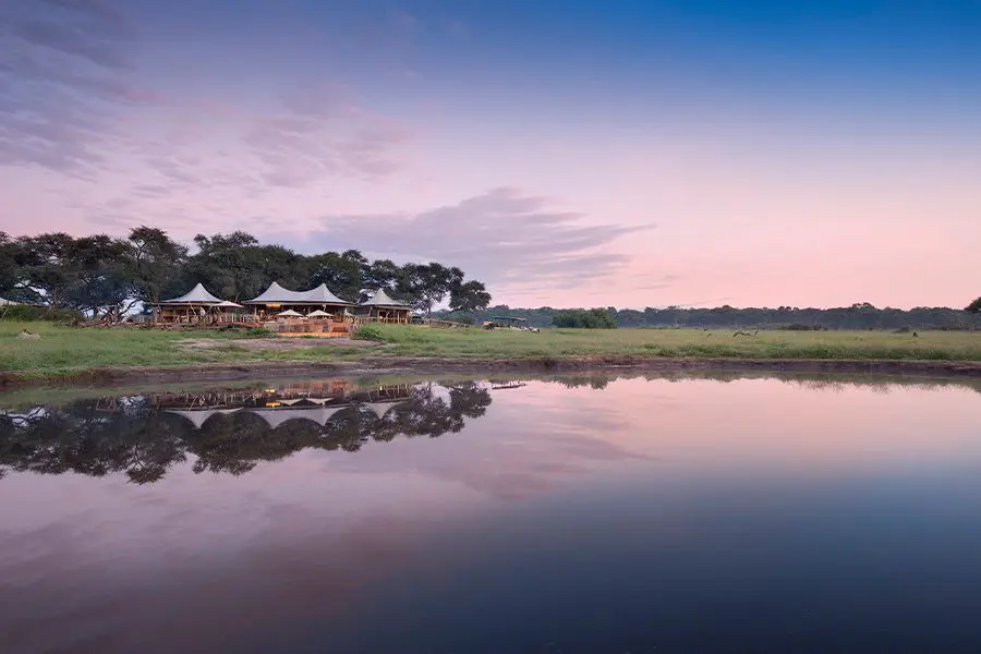 A large body of water reflects a pink sky with a view across to Somalisa Camp | Go2Africa