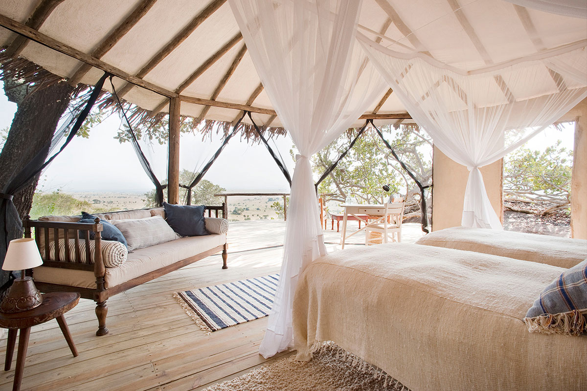 Twin beds with gathered mosquito nets and various wood furniture items overlook the suite's balcony and surrounding bush | Go2Africa