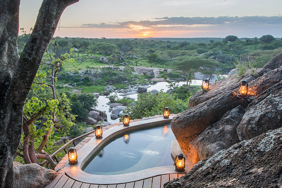 A plunge pool built into the side of a boulder with lanterns around the edge overlooks a jurassic-like landscape and across to the sunset | Go2Africa