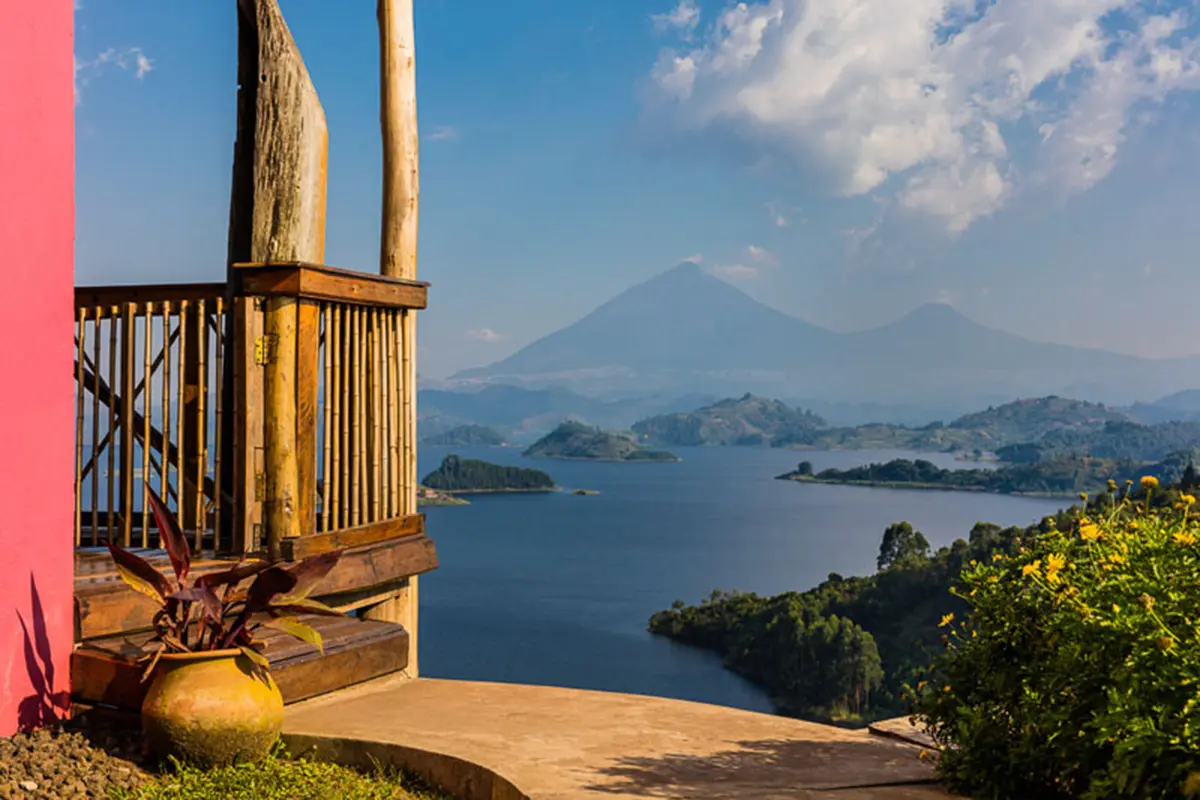 A small amount of red wall and a balcony extending from Chameleon Hills Lodge in Uganda overlook a large body of water and over to mountains beyond | Go2Africa