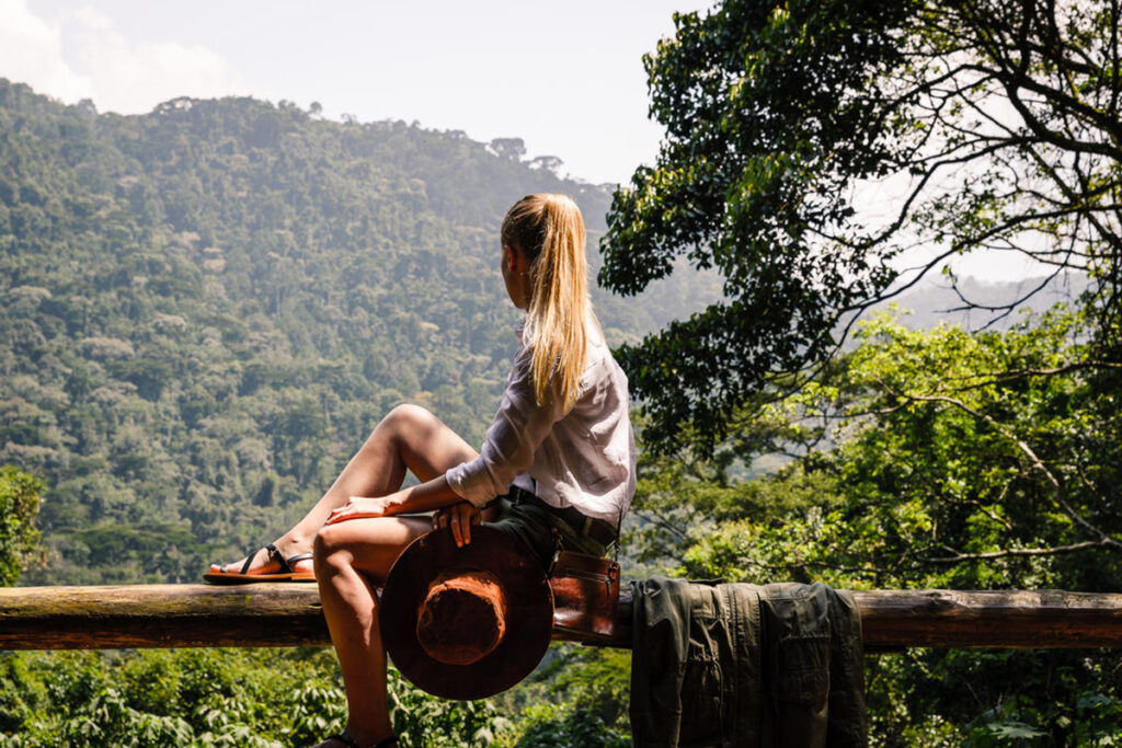 A woman sitting on a wooden beam overlooking part of a forest in Uganda | Go2Africa