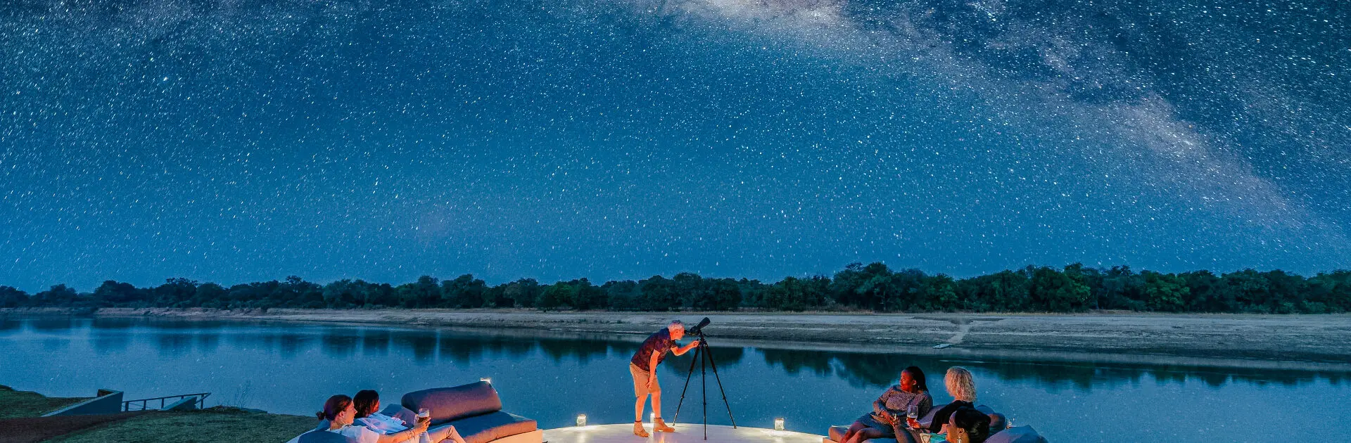 Un grupo sentado en una boma alrededor de una hoguera junto a una masa de agua con un telescopio mirando las estrellas | Go2Africa