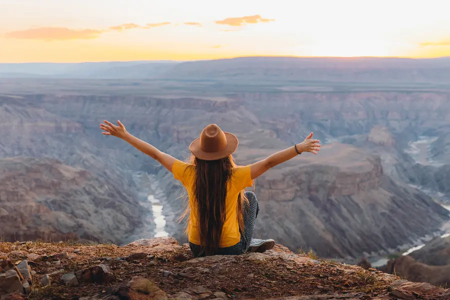 A woman sits at a viewpoint above the Fish River Canyon with her arms stretched out | Go2Africa