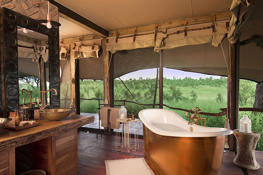A standalone bath and vanity look through the side of a tent out to a veranda and onto the bush beyond at Somalisa Camp | Go2Africa