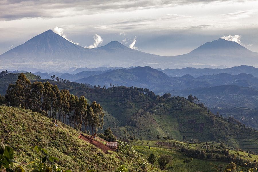 Small African farm cottage set on the side of hill with Volcanoes National Park in Rwanda in the background