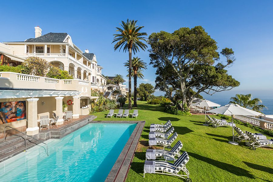 A long pool with loungers sit in front of a large manor house with views of the ocean in Cape Town, South Africa | Go2Africa