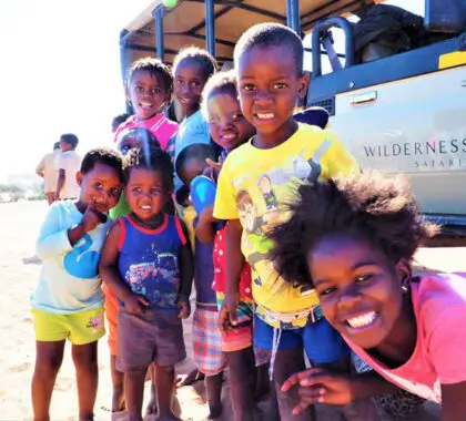 Children smiling while standing in front of a safari vehicle in Namibia.