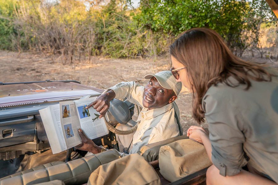 Safari guide teaches guest about spotting birds on a game drive in Lower Zambezi National Park, Zambia.