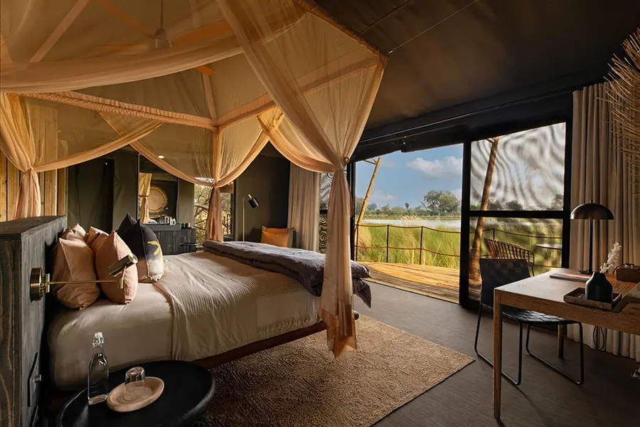 Vista de una suite del campamento North Island Okavango con cama con dosel y terraza con vistas a la exuberante vegetación y al agua | Go2Africa