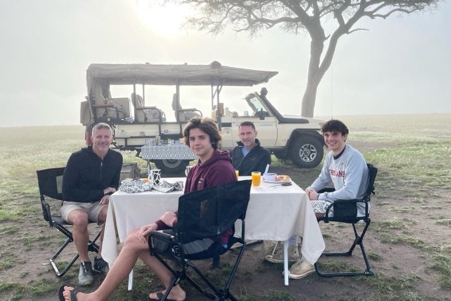 Gay couple and their teenage sons sit down for breakfast in front of a safari vehicle while in Africa.