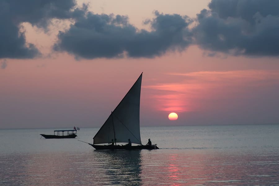 A dhow cruises the ocean at sunset off the coast of Zanzibar, Tanzania.