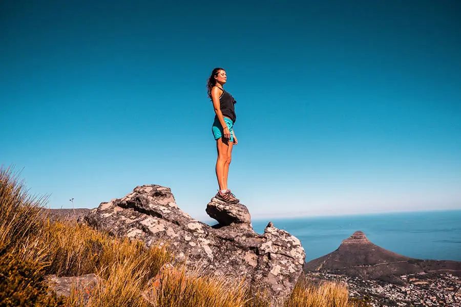 Una mujer en lo alto de una roca con Lion's Head al fondo en Ciudad del Cabo, Sudáfrica. 