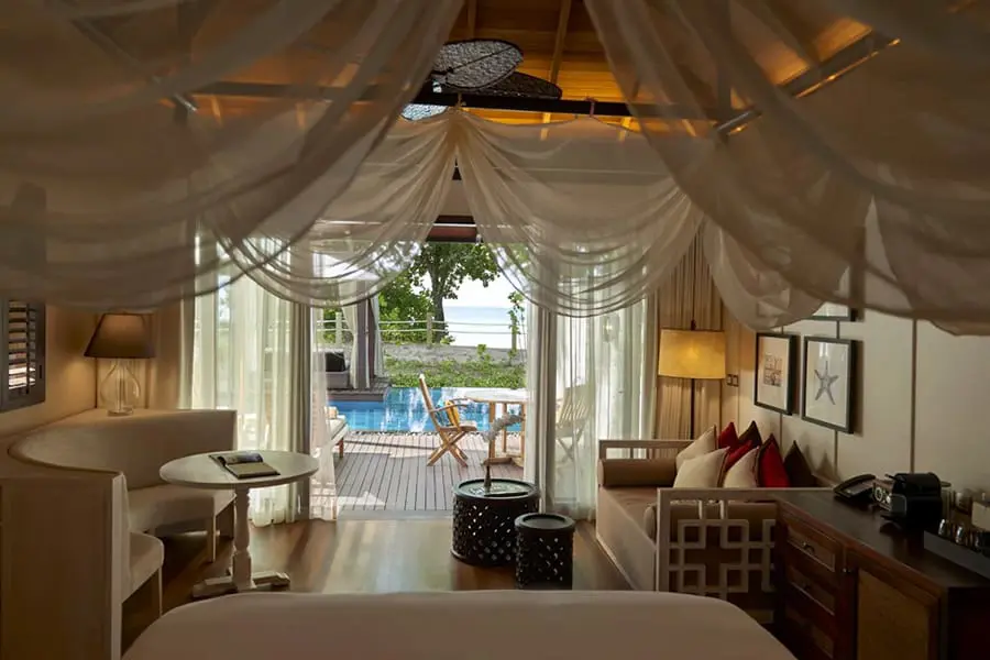 Looking out from a 4-poster bed onto a cosy lounge and further onto a wooden deck and plunge pool | Go2Africa