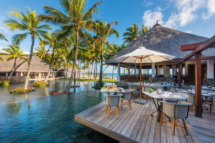 Una terraza de madera que se extiende desde un restaurante, con mesas y sombrillas, se cierne sobre una masa de agua salpicada de palmeras e islotes | Go2Africa