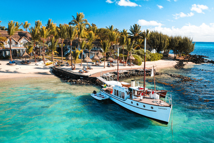 A boat, beach, and palm trees with 20 Degrees Sud hotel in the background | Go2Africa