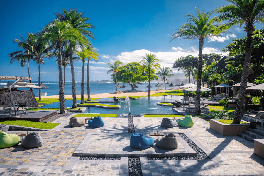 Bancos de arena y palmeras alrededor de una piscina junto a la playa con vistas a palapas de paja más abajo | Go2Africa