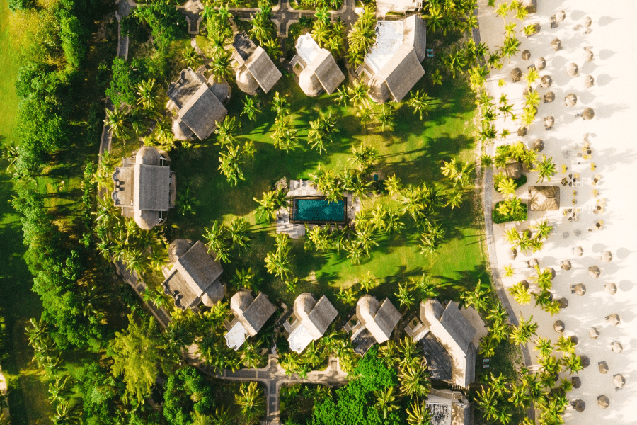 An aerial view showing a crescent of thatched accommodations and a pool leading on to a beach at Dinarobin Beachcomber Golf Resort & Spa | Go2Africa