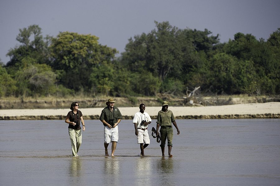 Four people crossing a body of water while on a walking safari in South Luangwa National Park | Go2Africa