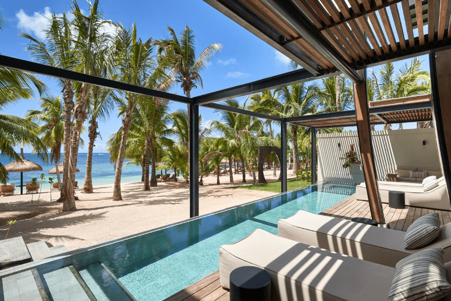 Loungers in front of a pool directly by the beach with palm trees and palapas at LUX* Grand Baie in Mauritius | Go2Africa