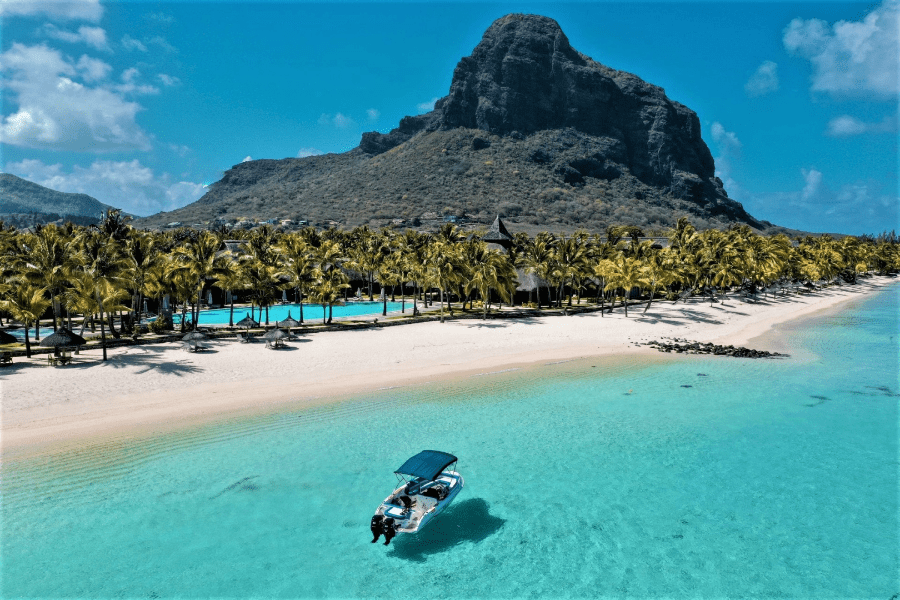 Un barco flota cerca de una playa frente al Paradise Beachcomber Gold Resort & Spa mirando hacia la montaña Le Morne | Go2Africa