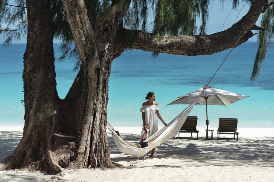 A woman standing on the beach by someone else lying in a hammock overlooking the cerulean ocean | Go2Africa