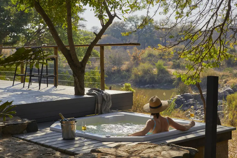 A woman sits in a plunge pool / hot tub overlooking the river from Toro River Lodge | Go2Africa