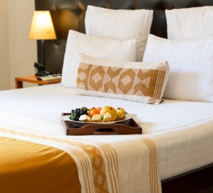 A close up of a bed with a platter of fruit with a lit lamp in the background | Go2Africa
