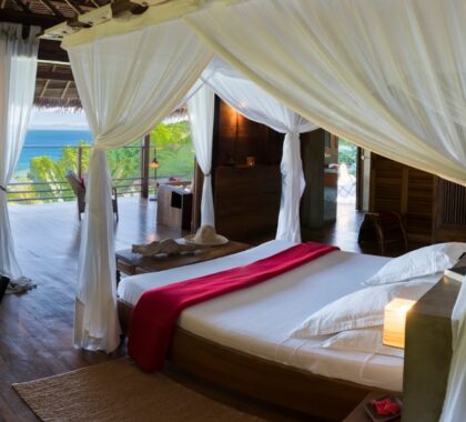 A four-poster bed with mosquito nets with a veranda looking over the ocean | Go2Africa
