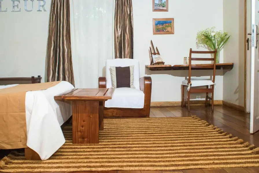 A small table, chair, end of bed wooden storage and the last part of a bed with a mustard coloured throw | Go2Africa