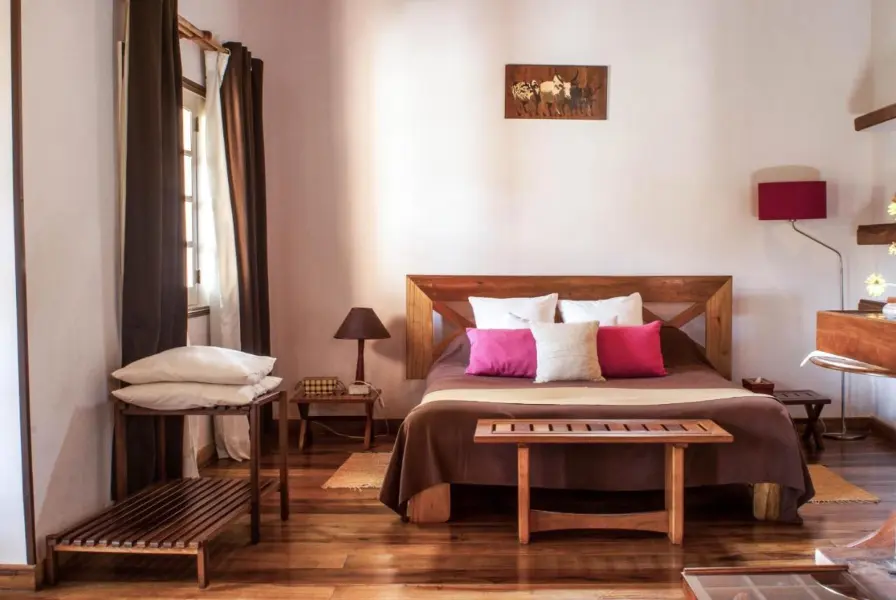 Warm wood, cream and brown accents through a bedroom with pops of bright pink in pillows and a standing lamp | Go2Afroca