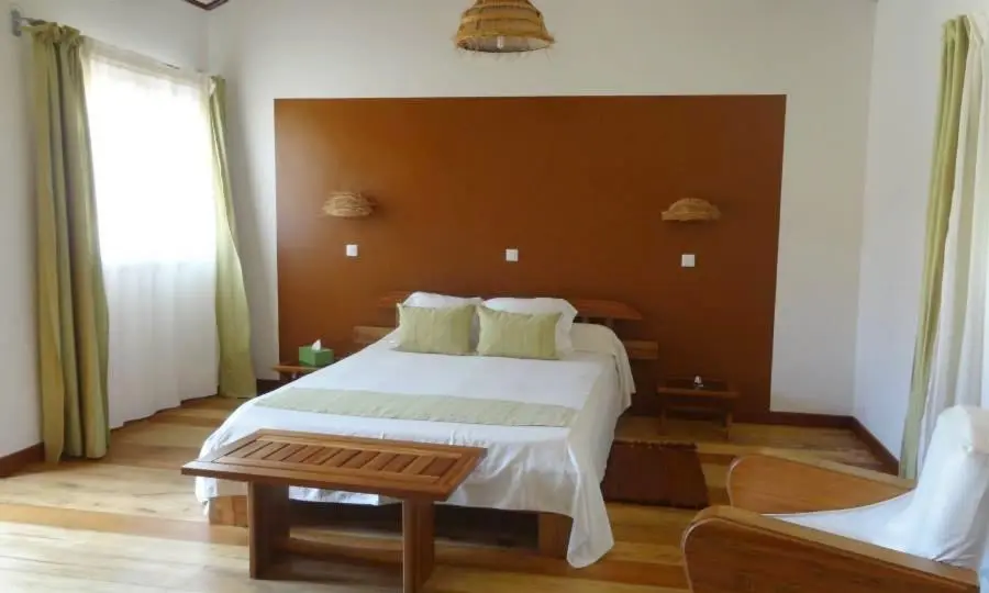 A white walled bedroom with a tan rectangle painted against the far wall behind the bed with green accents throughout | Go2Africa