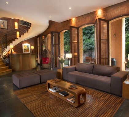 A modern lounge with wood finishes and a swooping staircase with windows that look out onto a garden | Go2Africa