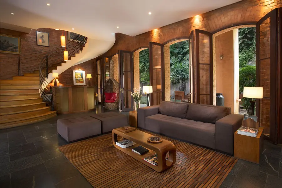 A modern lounge with wood finishes and a swooping staircase with windows that look out onto a garden | Go2Africa