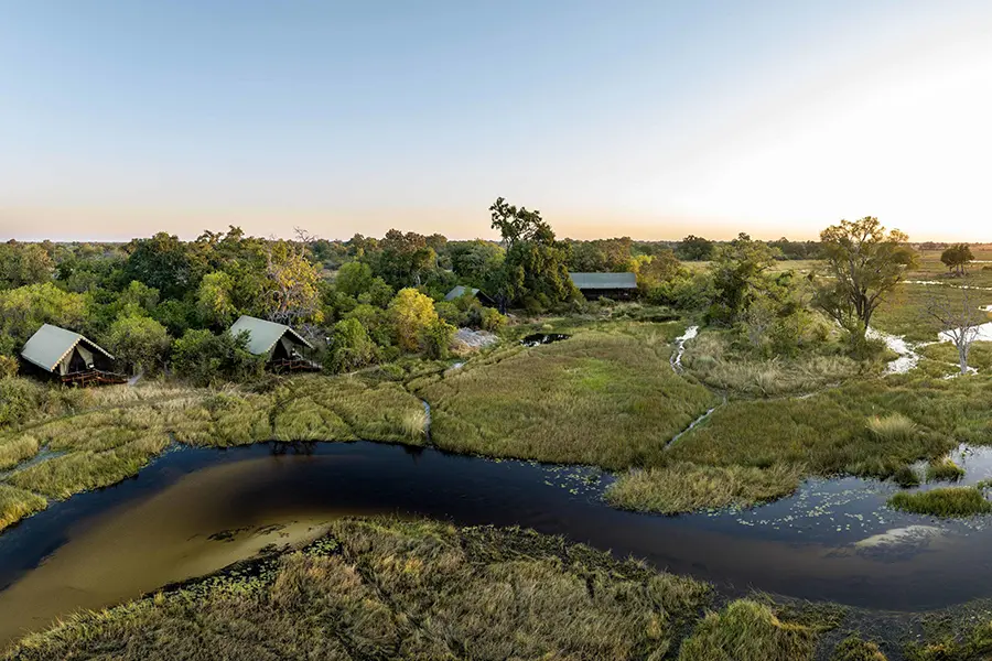Varias estructuras en forma de cabaña y un campamento principal se asientan entre los árboles de una vía fluvial en el delta del Okavango | Go2Africa