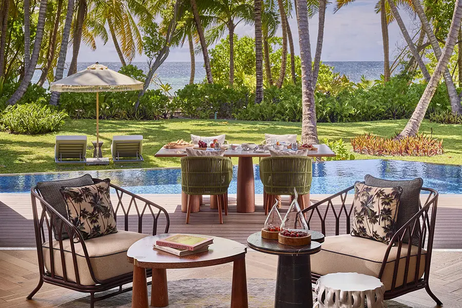 A cosy seating area with a dining table in the background looking over a pool on the deck, palm trees, and over to the ocean | Go2Africa