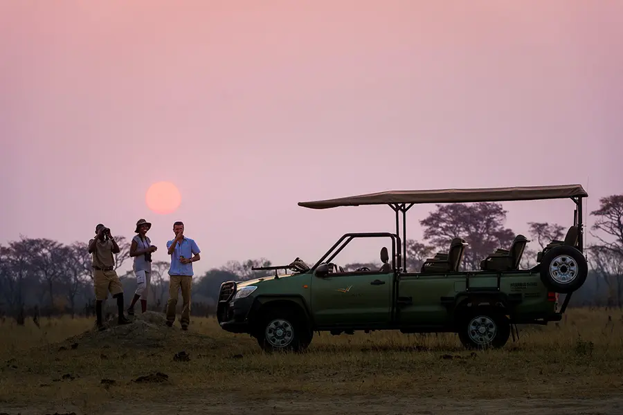 Huéspedes disfrutan de una puesta de sol durante un safari cerca del campamento Linkwasha en Hwange, Zimbabue.