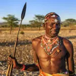 Guerrero africano de la tribu Samburu de pie en la sabana y sosteniendo una lanza en el centro de Kenia. 