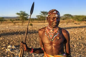 Guerrero africano de la tribu Samburu de pie en la sabana y sosteniendo una lanza en el centro de Kenia. 