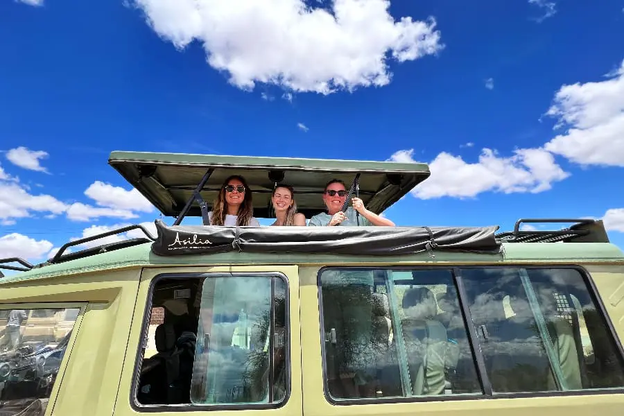 Three woman pop their heads out the rooftop viewing area of a game vehicle while waiting to set off | Go2Africa