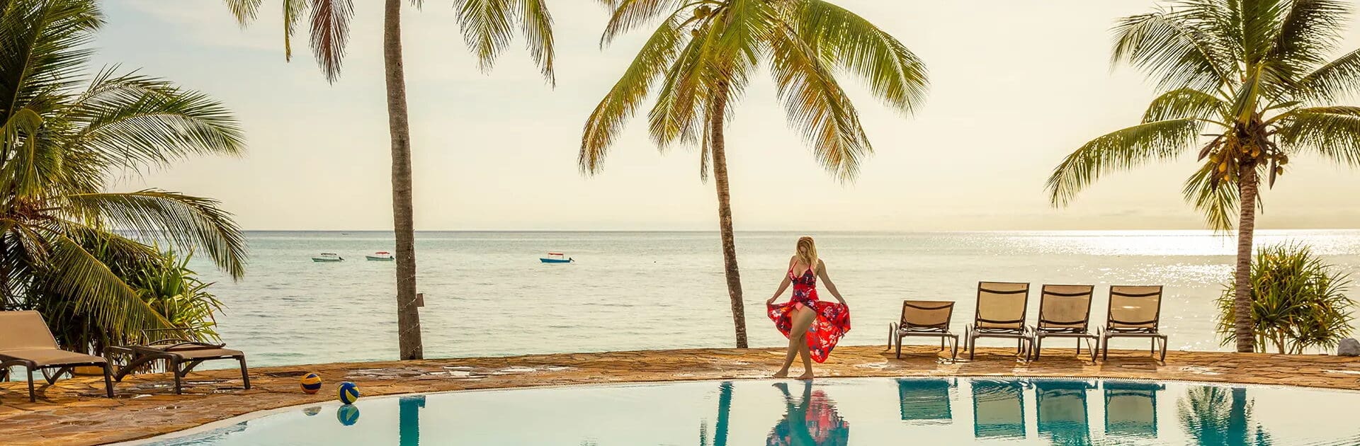 Mujer con vestido rojo paseando alrededor de una piscina rodeada de palmeras en unas vacaciones tropicales en Zanzíbar, Tanzania | Go2Africa