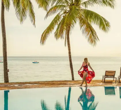 Mujer con vestido rojo paseando alrededor de una piscina rodeada de palmeras en unas vacaciones tropicales en Zanzíbar, Tanzania | Go2Africa