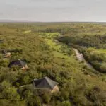 Las tiendas de campaña están escondidas entre los árboles, cerca de un río caudaloso.