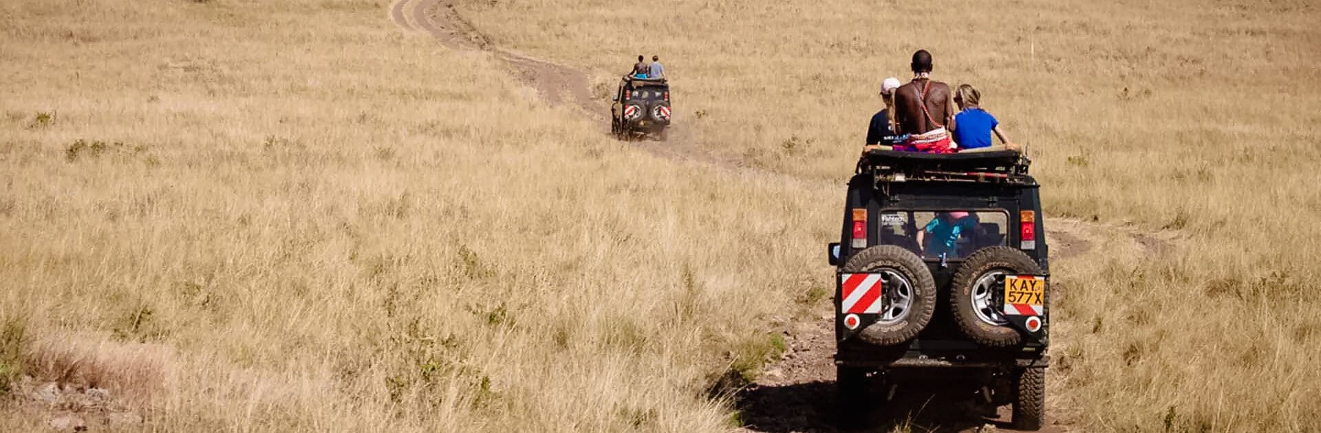Two game vehicles with guests and guides drive away from the camera on savannah like plains | Go2Africa