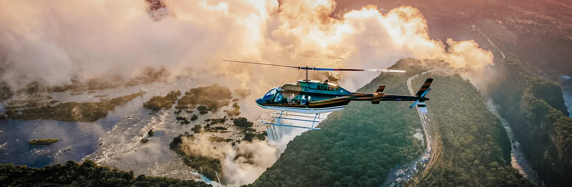 Un vuelo en helicóptero sobre las cataratas Victoria, con el chorro de agua en erupción al fondo y el resplandor anaranjado de la luz del sol a través de la niebla | Go2Africa