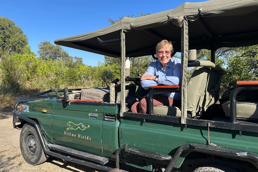 Uma senhora encostada à lateral de um veículo de safari Feline Fields a olhar para a câmara | Go2Africa