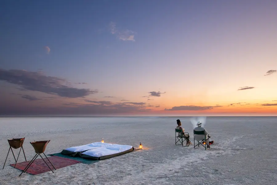 Ein Paar starrt auf den Sonnenuntergang über einer weißen Salzpfanne in Botswana mit ihren Schlafsäcken im Rücken | Go2Africa