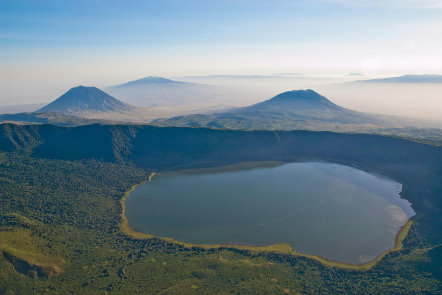 Circular crater with a soda lake at its centre, surrounded by steep forested slopes by The Highlands, Asilia | Go2Africa