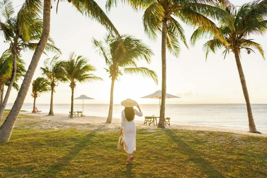 Woman walking towards a beach lined with palm trees at sunset | Go2Africa