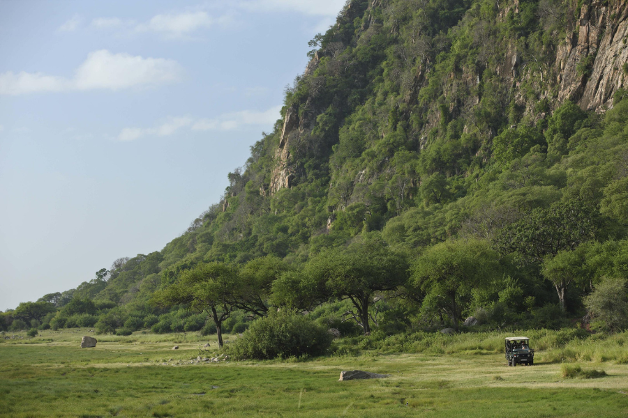 Safari vehicle driving across grassy terrain near steep, forested crater walls | Go2Africa